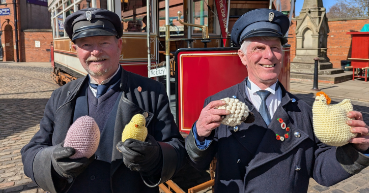 Two men in period tram driver costumes holding easter items at Beamish Museum.